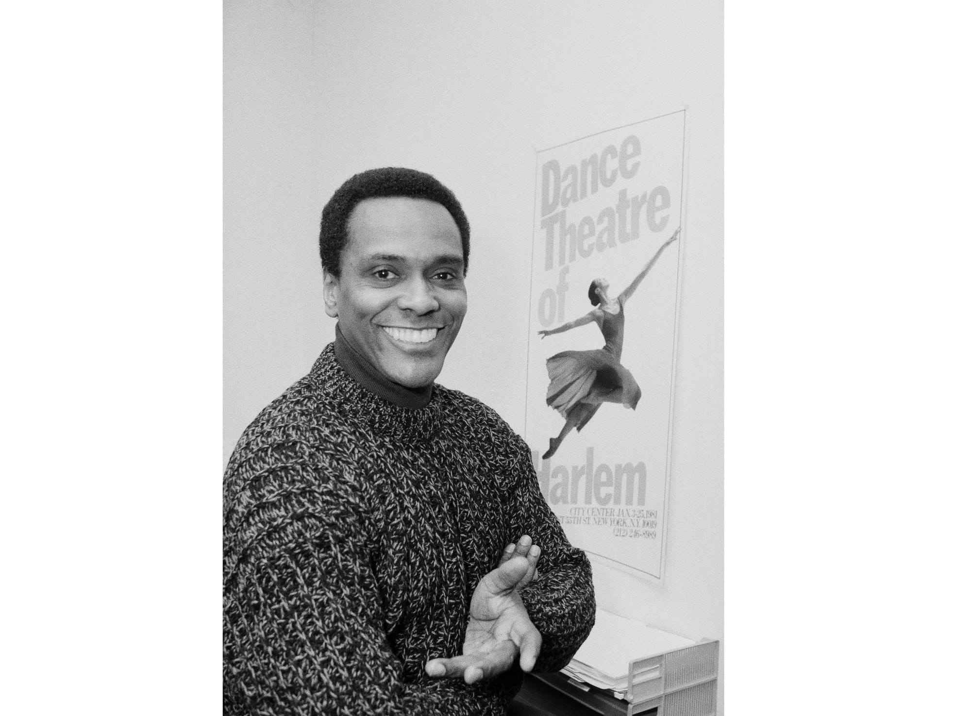 Arthur Mitchell sitting next to a poster for the Dance Theatre of Harlem