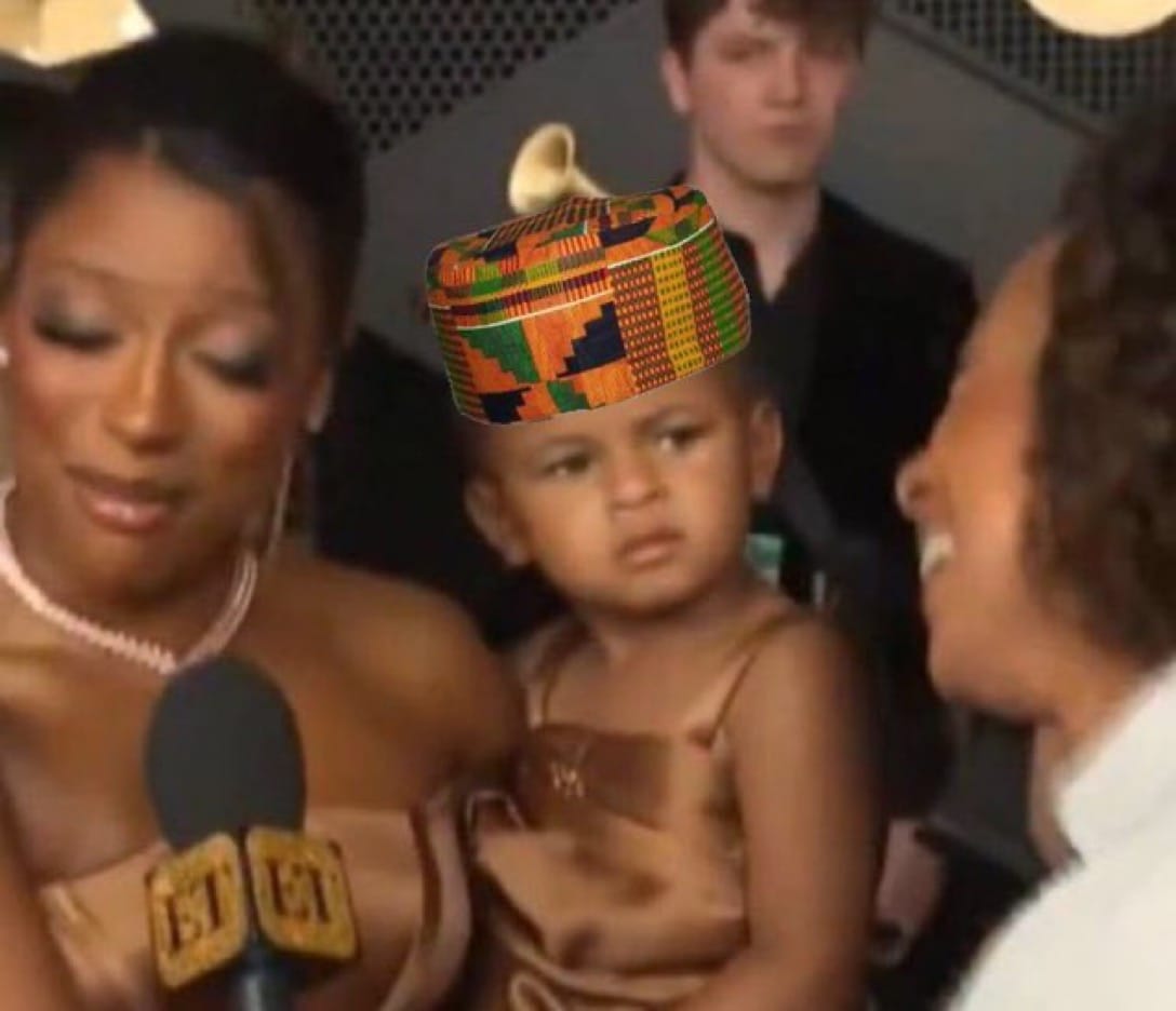 Victoria Monet holds baby Hazel, who is wearing a kente kufi and staring quizzically.
