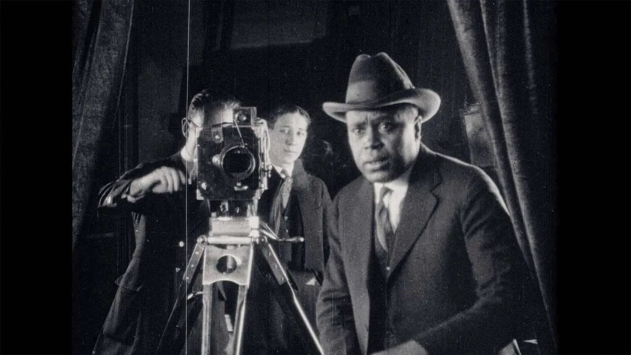 A black and white photo of the filmmaker Oscar Micheaux directing a film with his crew behind him