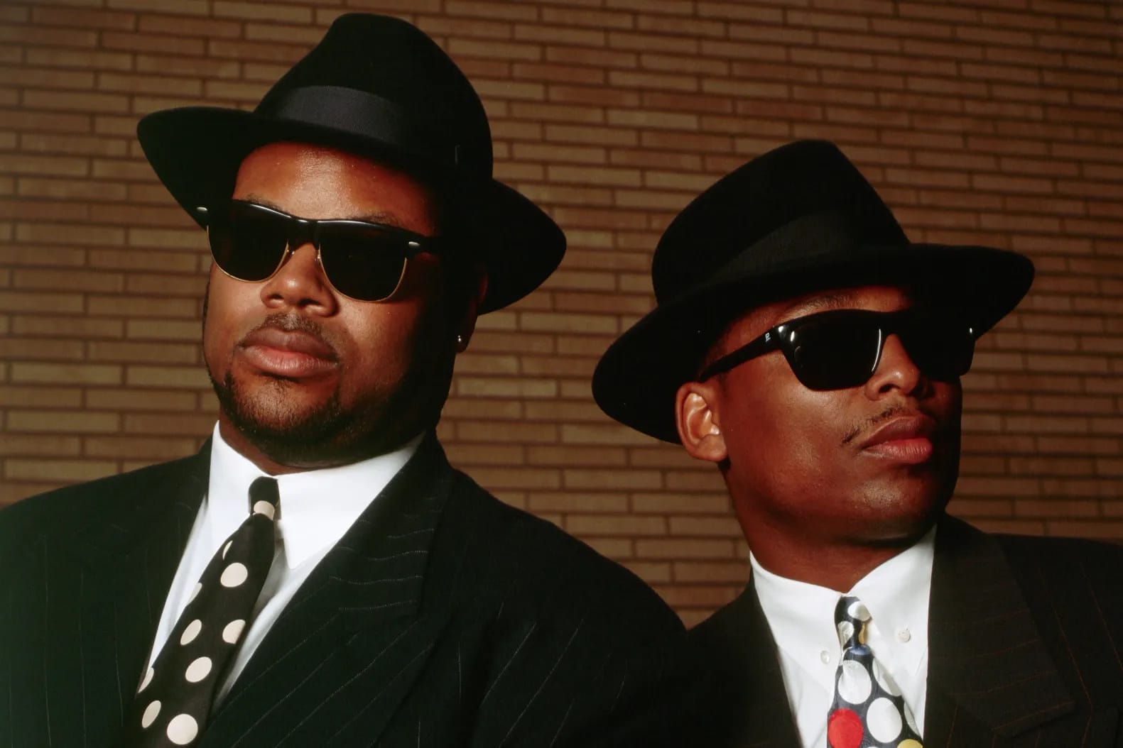 a portrait of Jimmy Jam and Terry Lewis in their customary black fedora, black sunglasses, and black suits