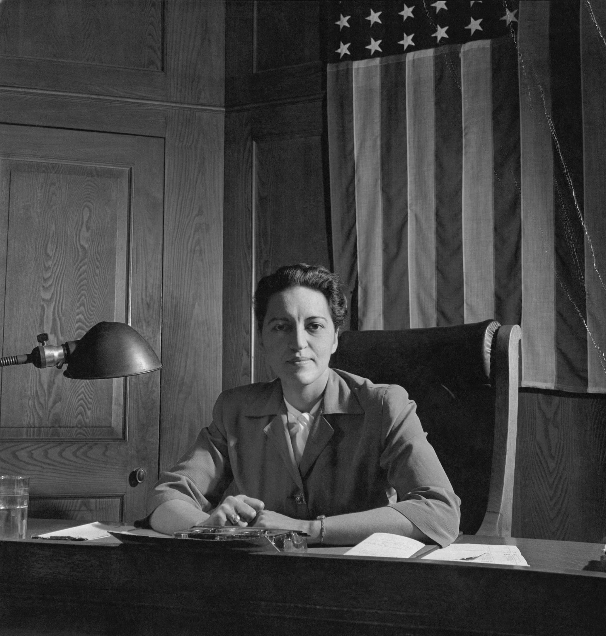 A black and white photo of Jane Bolin sitting behind her desk in front of an American flag