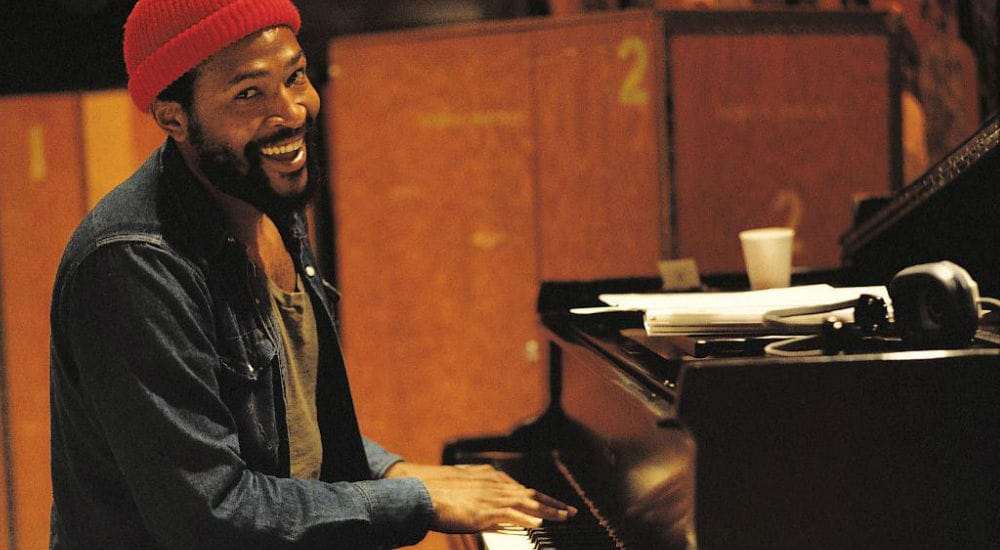 a photo of marvin gaye sitting and playing the piano while he wears his customary orange beanie