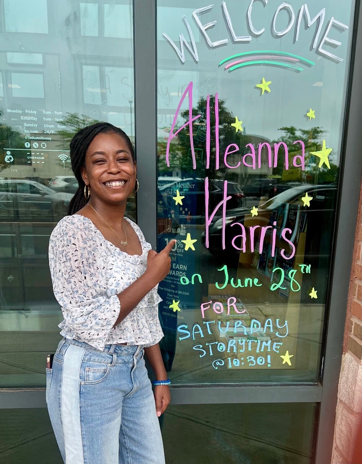 Alleanna Harris points at the beautiful welcome sign for Saturday Storytime on B&N Hamilton's window.